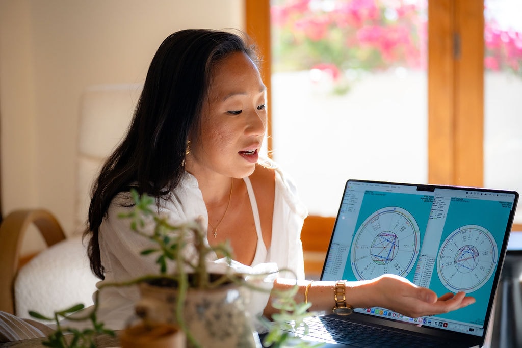 Victoria explaining astrology charts on a laptop at a sunlit table